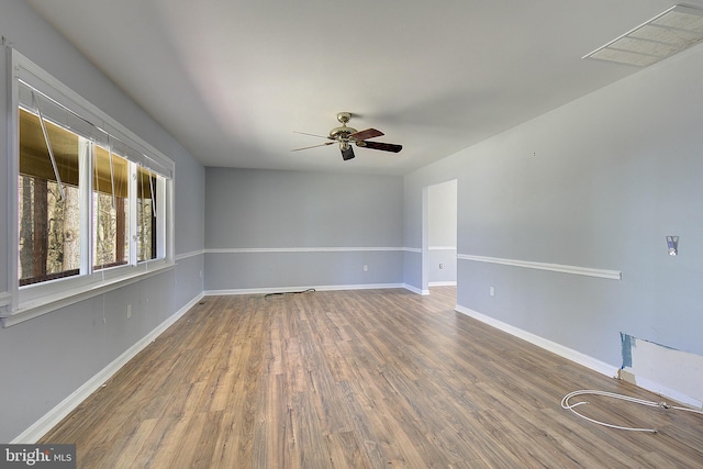 empty room with ceiling fan, visible vents, baseboards, and wood finished floors