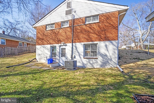 rear view of house with central AC, fence, brick siding, and a lawn