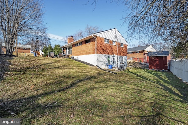 rear view of property with an outbuilding, a storage shed, fence, a lawn, and a chimney