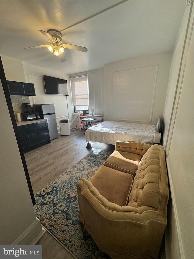 bedroom with a ceiling fan, wood finished floors, and freestanding refrigerator