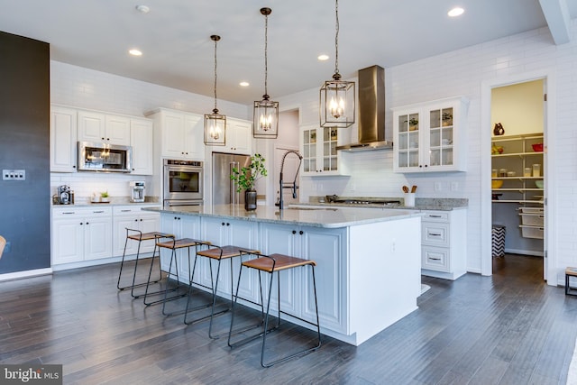 kitchen featuring a kitchen breakfast bar, wall chimney range hood, white cabinets, and appliances with stainless steel finishes