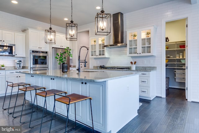 kitchen with dark wood finished floors, appliances with stainless steel finishes, white cabinets, wall chimney exhaust hood, and a sink