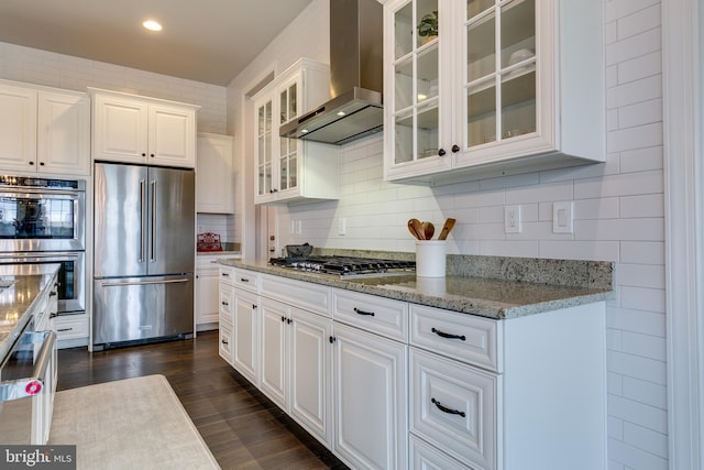 kitchen featuring dark wood-type flooring, stainless steel appliances, white cabinets, wall chimney range hood, and decorative backsplash