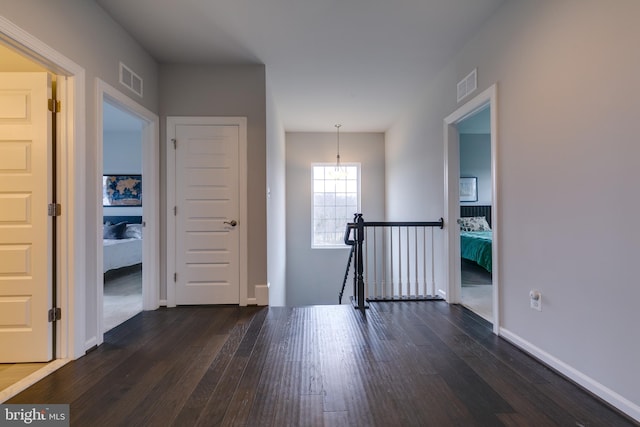 hall with dark wood-style floors, an upstairs landing, and visible vents