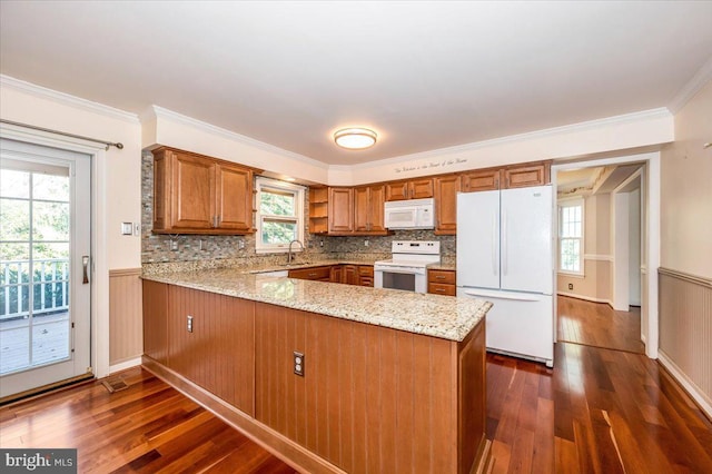 kitchen with a wainscoted wall, dark wood-style floors, white appliances, a peninsula, and brown cabinetry