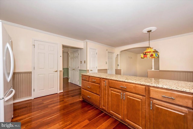 kitchen featuring light stone countertops, dark wood-style floors, freestanding refrigerator, wainscoting, and brown cabinets