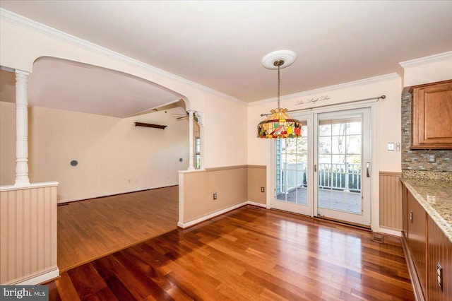 unfurnished dining area with crown molding, ceiling fan, wainscoting, wood finished floors, and arched walkways