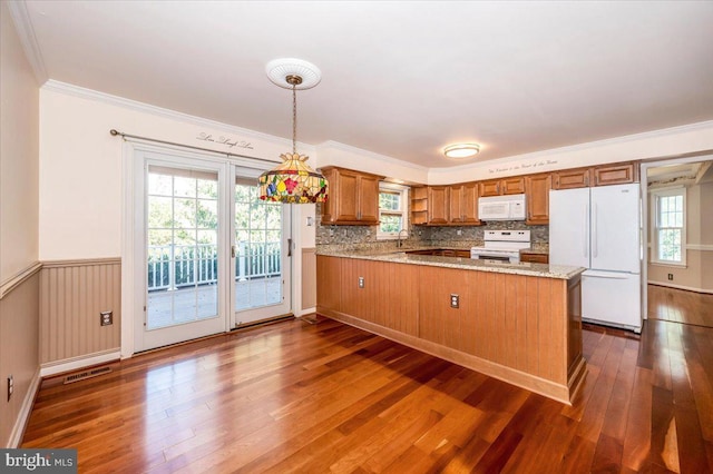 kitchen with a wainscoted wall, white appliances, brown cabinets, and a peninsula