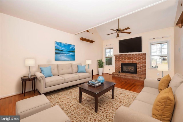 living area featuring a fireplace, lofted ceiling, wood finished floors, and a healthy amount of sunlight