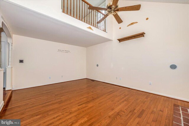 empty room with a ceiling fan, wood finished floors, baseboards, and a towering ceiling