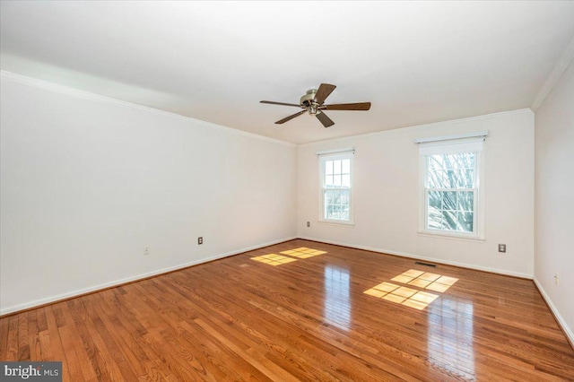 empty room with visible vents, ornamental molding, baseboards, and wood-type flooring