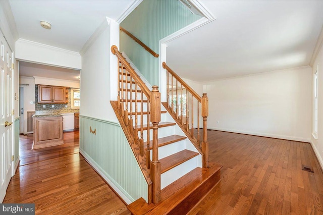 staircase featuring wood finished floors, visible vents, and ornamental molding