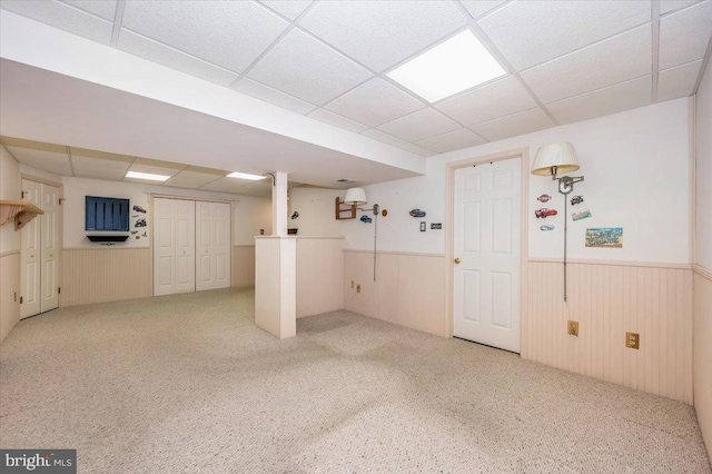 finished below grade area with a drop ceiling, carpet floors, wooden walls, and wainscoting