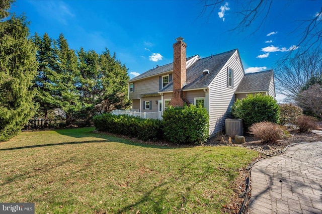 view of side of home with a lawn, roof with shingles, a chimney, and fence