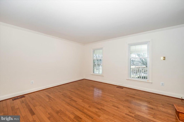 spare room featuring visible vents, crown molding, baseboards, and hardwood / wood-style floors