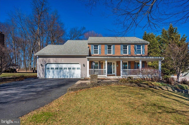 colonial-style house with an attached garage, covered porch, a front lawn, aphalt driveway, and brick siding