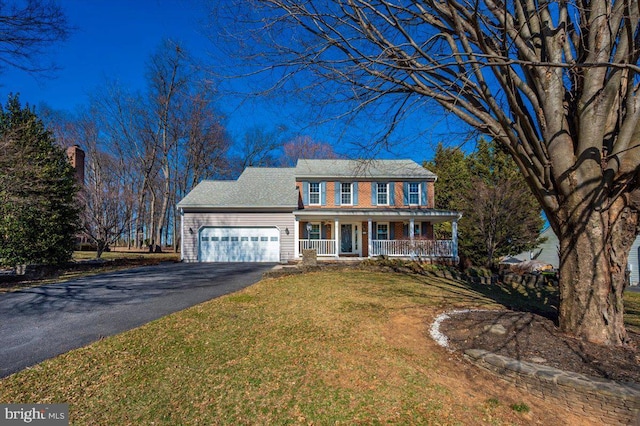 colonial house with aphalt driveway, covered porch, a front yard, an attached garage, and brick siding