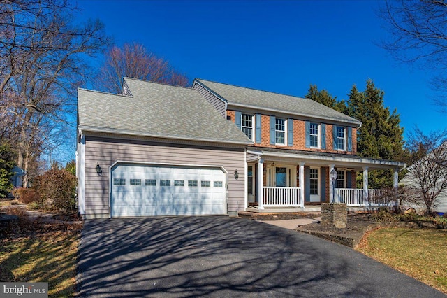 colonial-style house with aphalt driveway, a porch, a shingled roof, a garage, and brick siding