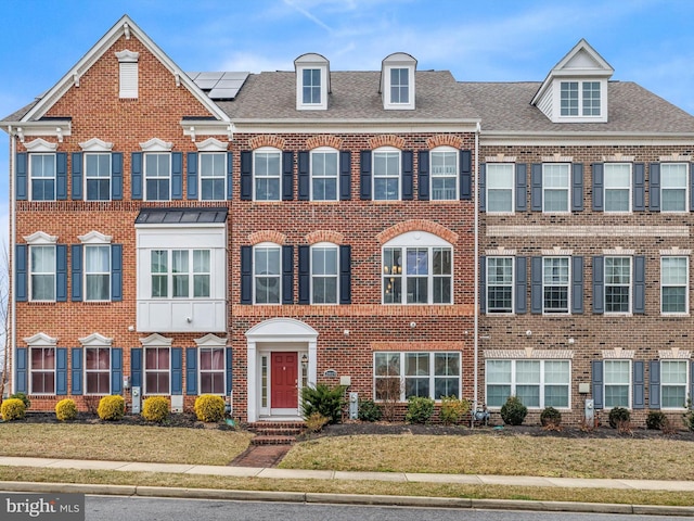 townhome / multi-family property with a shingled roof, roof mounted solar panels, and brick siding