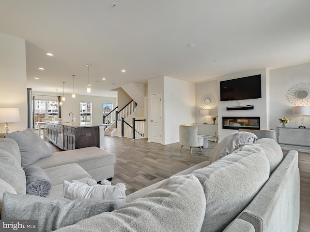 living room featuring a glass covered fireplace, wood finished floors, recessed lighting, and stairs