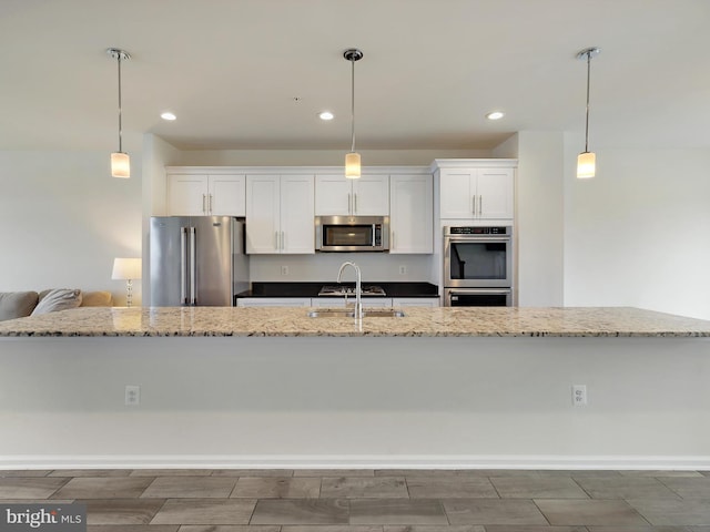 kitchen with stainless steel appliances, white cabinets, a sink, and hanging light fixtures