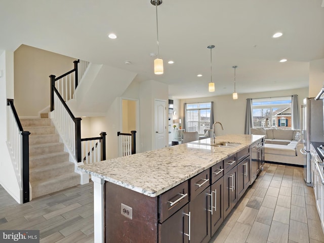 kitchen featuring a center island with sink, dark brown cabinets, wood finish floors, a sink, and recessed lighting