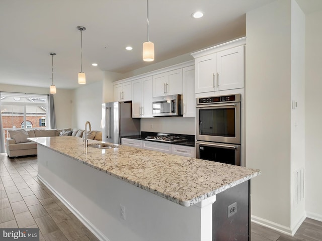 kitchen with stainless steel appliances, a kitchen island with sink, a sink, and white cabinetry