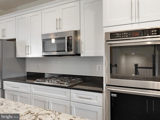 kitchen featuring dark stone counters, appliances with stainless steel finishes, and white cabinetry