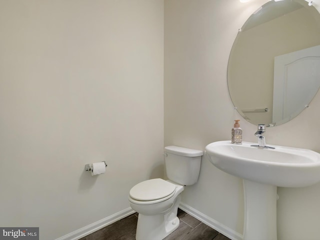 half bath featuring toilet, a sink, baseboards, and wood finished floors