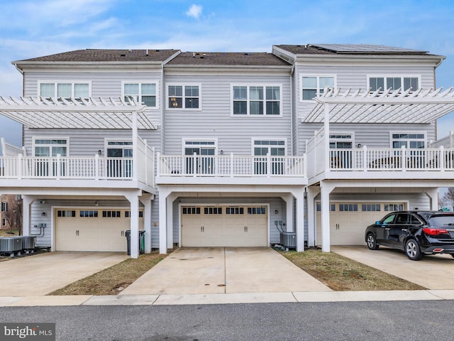 view of front of home with an attached garage, central air condition unit, driveway, and a pergola