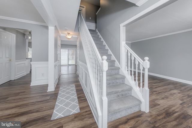 staircase with ornamental molding, a wainscoted wall, a decorative wall, and wood finished floors