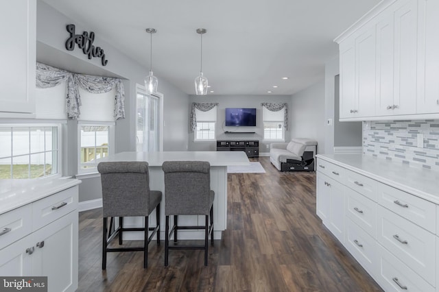 kitchen featuring dark wood-style flooring, white cabinetry, a breakfast bar, and backsplash