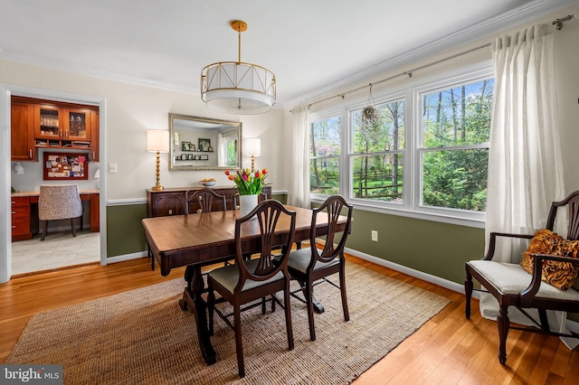 dining space with ornamental molding, light wood finished floors, and baseboards