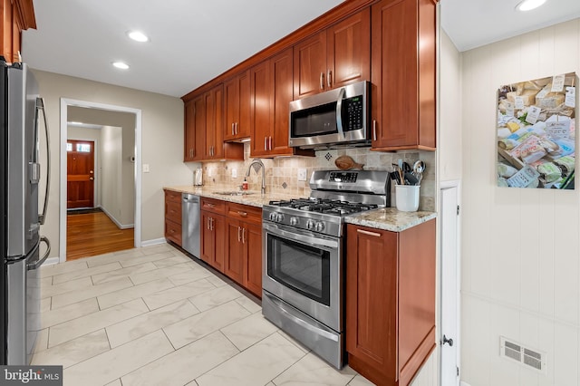 kitchen featuring a sink, light stone counters, stainless steel appliances, and tasteful backsplash