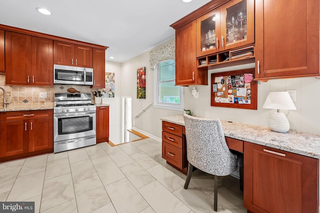 kitchen with appliances with stainless steel finishes, light stone countertops, built in desk, and backsplash
