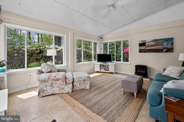 tiled living area featuring vaulted ceiling, plenty of natural light, a wood stove, and baseboards