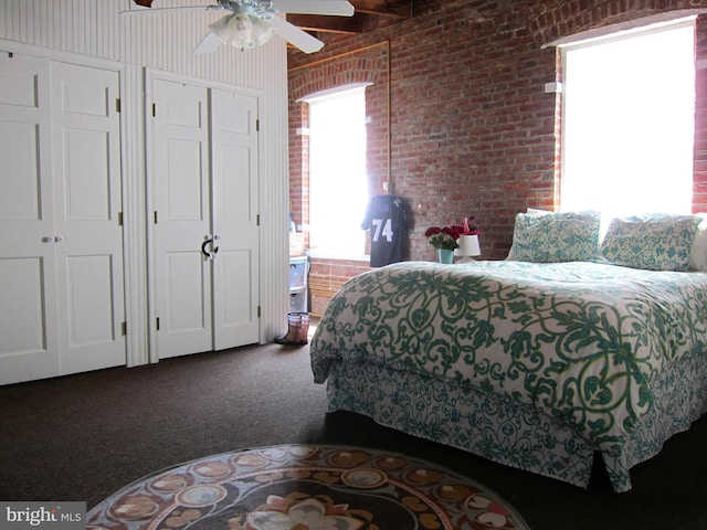 carpeted bedroom with two closets, a ceiling fan, and brick wall