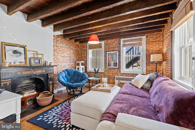 living area with radiator, brick wall, beam ceiling, a fireplace, and hardwood / wood-style flooring