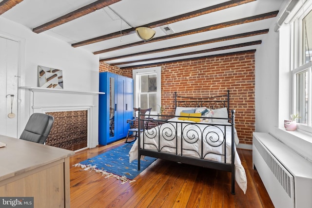 bedroom with radiator, brick wall, a fireplace, wood-type flooring, and beamed ceiling