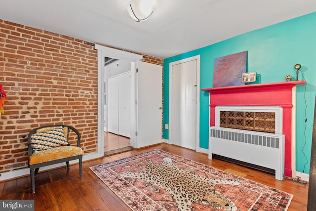 interior space with hardwood / wood-style flooring, radiator, baseboards, and brick wall