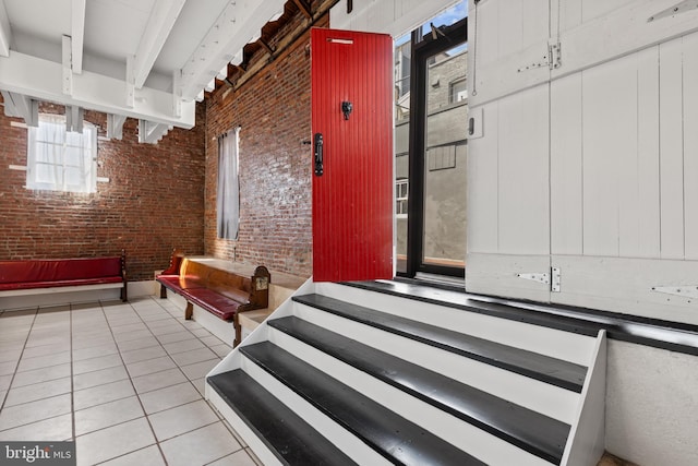 interior space featuring tile patterned floors, beam ceiling, and brick wall