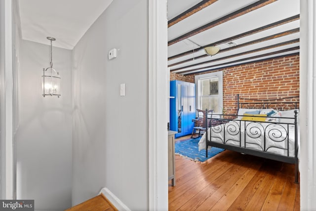 corridor featuring beam ceiling, a chandelier, brick wall, and hardwood / wood-style floors