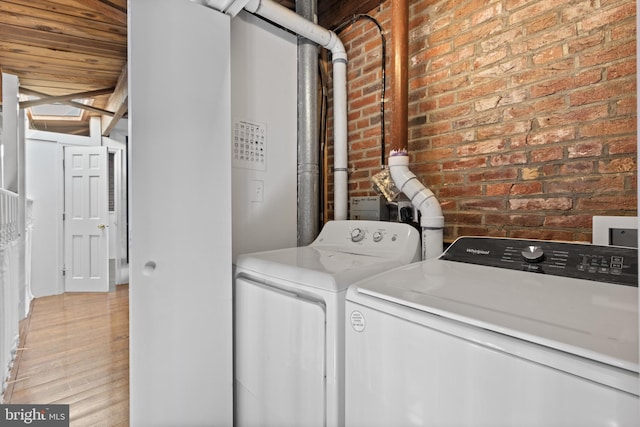 washroom with washing machine and clothes dryer, brick wall, and wood finished floors