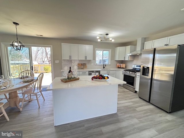 kitchen featuring wall chimney range hood, a notable chandelier, backsplash, and stainless steel appliances