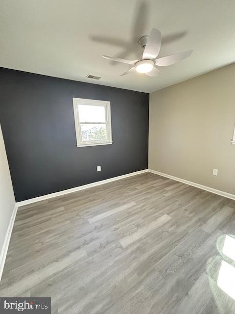 empty room featuring ceiling fan, visible vents, baseboards, and wood finished floors