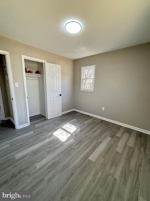 unfurnished bedroom with baseboards, dark wood-style flooring, and a closet