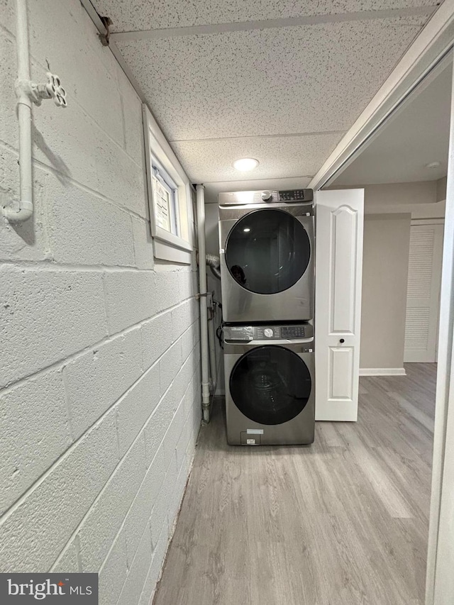 washroom featuring laundry area, concrete block wall, stacked washer / drying machine, and wood finished floors