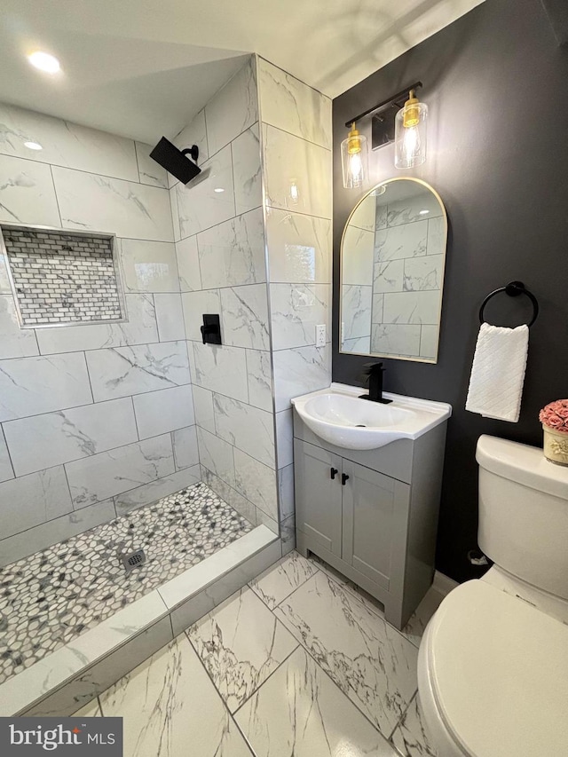 full bath featuring a tile shower, marble finish floor, toilet, and vanity