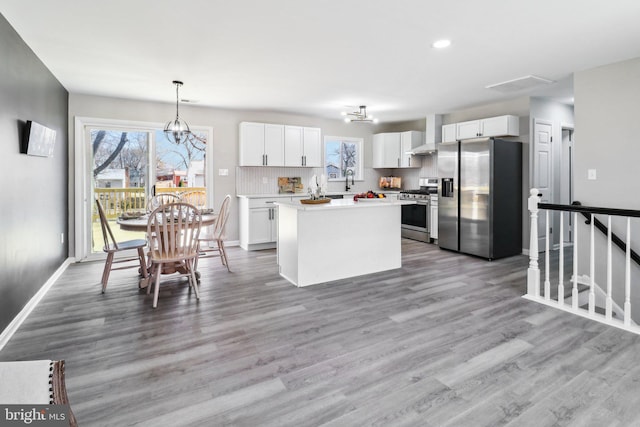 kitchen with stainless steel appliances, decorative backsplash, white cabinetry, wall chimney range hood, and a chandelier