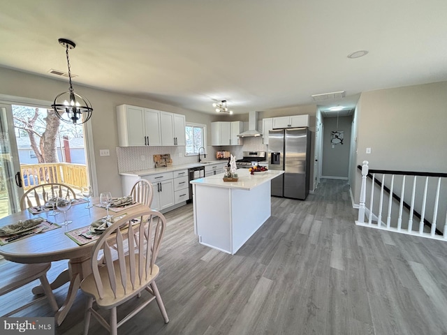 kitchen featuring visible vents, decorative backsplash, stainless steel appliances, wall chimney exhaust hood, and a sink